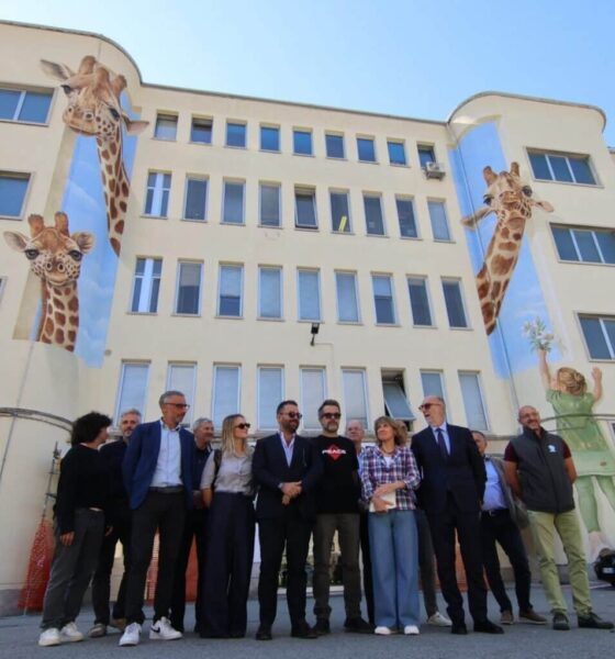 Foto di gruppo davanti al nuovo murales realizzato sulla facciata principale dell'Irccs materno infantile Burlo Garofolo di Trieste