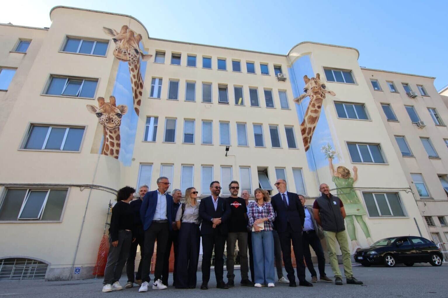 Foto di gruppo davanti al nuovo murales realizzato sulla facciata principale dell'Irccs materno infantile Burlo Garofolo di Trieste